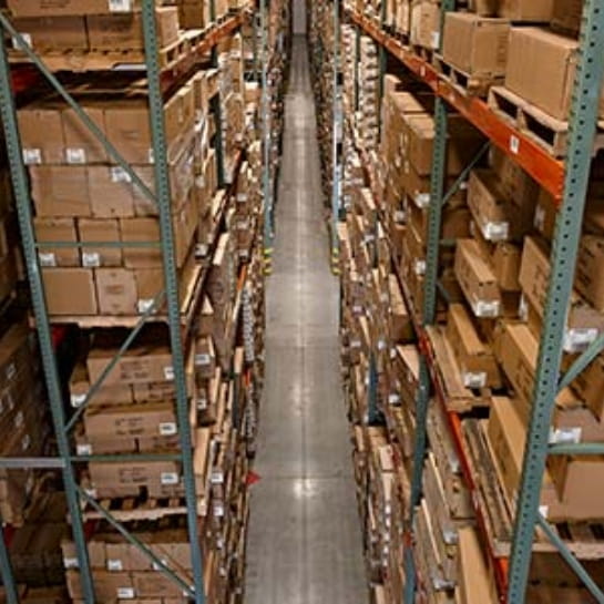 Overhead view of a warehouse aisle framed by green and red pallet racking fully stocked with boxed inventory