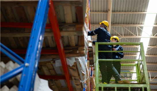Two workers in safety jumpsuits and hard hats using a scissor lift to install pallet racking in a warehouse facility