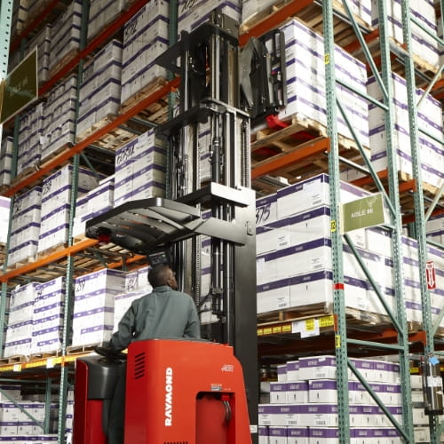 Worker operating a Raymond reach truck to place a pallet of boxed inventory into high-level warehouse racking