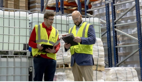Customer in a sport coat and safety vest reviewing marketing materials with a Raymond Storage Concepts representative in a warehouse aisle
