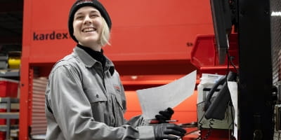 Raymond Storage Concepts warehouse employee smiling while reviewing a parts order with a Kardex Remstar vertical lift module in the background