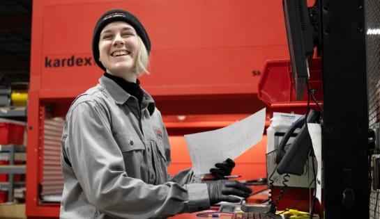 Raymond Storage Concepts warehouse employee smiling while reviewing a parts order with a Kardex Remstar vertical lift module in the background