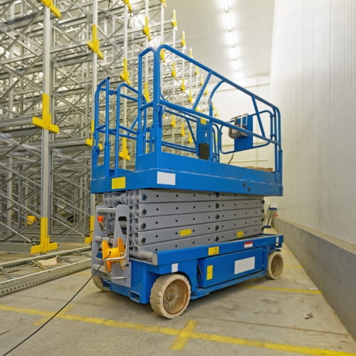 Blue scissor lift parked in a warehouse aisle with industrial metal racking in the background