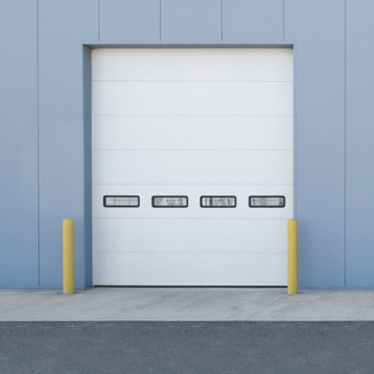 Sectional industrial garage door with four windows on the exterior wall of a warehouse building