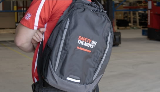 Raymond Storage Concepts team member in a red shirt wearing a Raymond Safety On The Move black backpack in a warehouse