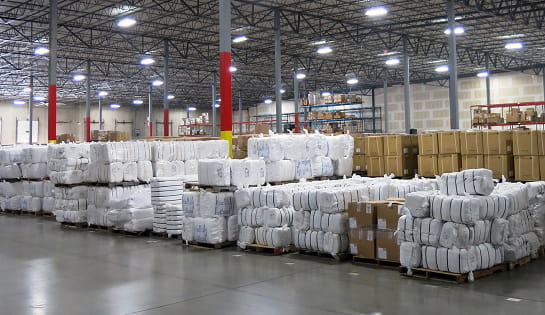 Before view of the Standard Textile storage area showing floor-stacked textile bales and carton pallets across the warehouse floor