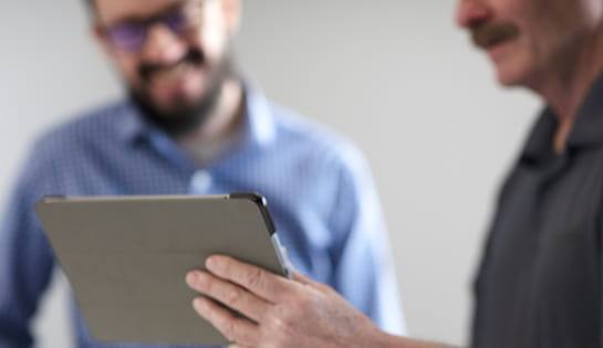 Team member holding a tablet with a colleague in blue working in the background of a warehouse