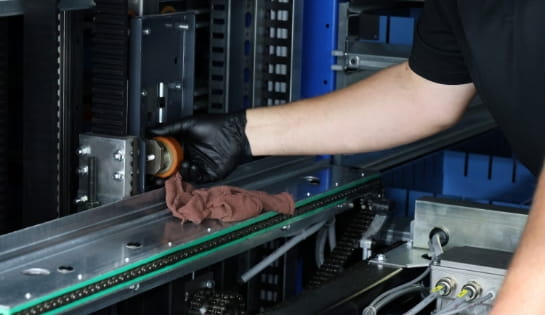 Gloved technician hand cleaning a wheel with a rag inside an automated storage and retrieval system