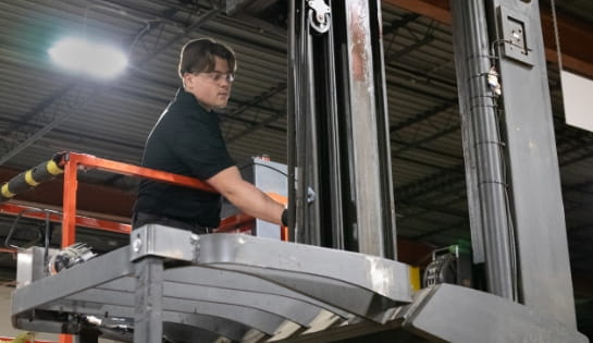 Raymond Storage Concepts shop technician on a scissor lift inspecting a forklift mast for safety and functionality