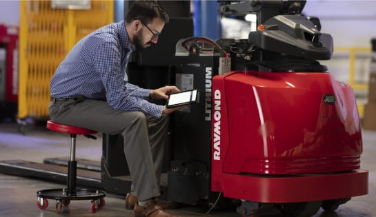 Raymond Storage Concepts representative holding a tablet to review an iBATTERY dashboard next to a Raymond forklift and battery