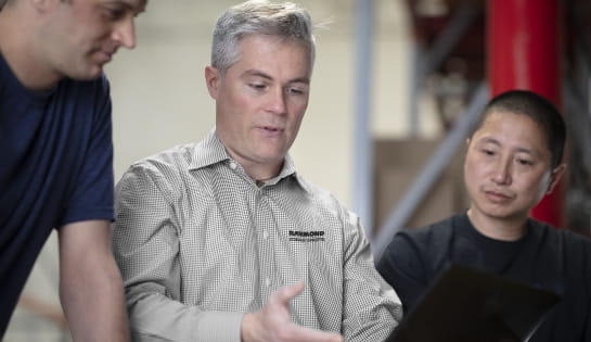 Raymond Storage Concepts employee showing something to two men during a collaborative discussion