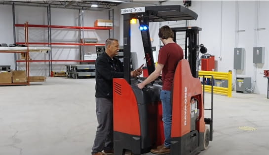 Raymond Storage Concepts trainer talking with a forklift operator trainee about forklift controls on a counterbalanced lift truck in a warehouse