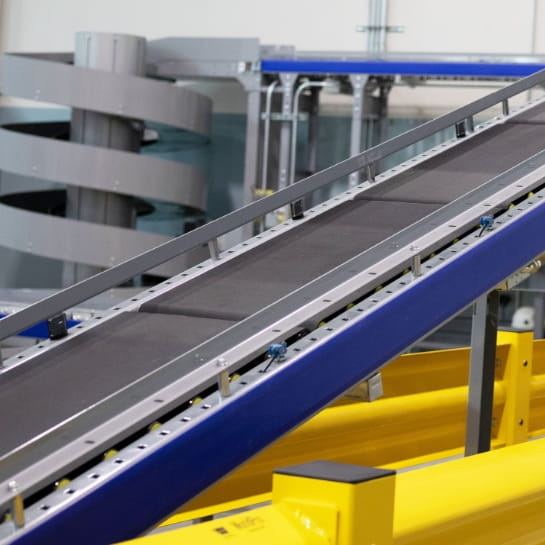 Angled upward conveyor ramp with an industrial conveyor screw in the background of a facility