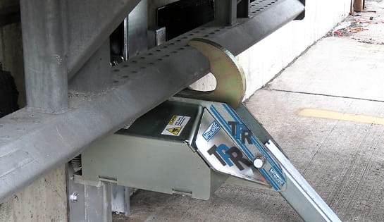 Close-up of a vehicle restraint securely hooked to the underride guard of a semi-truck at a loading dock