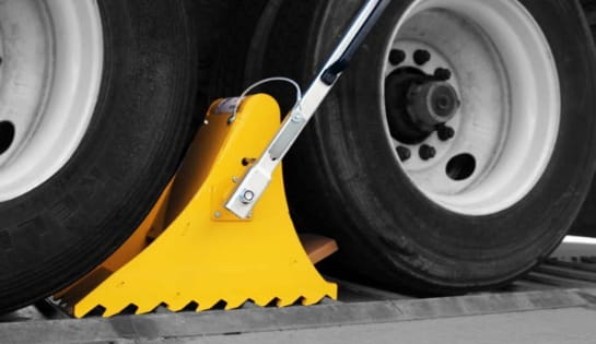 Close-up of truck wheels secured with a high-visibility yellow wheel restraint at a loading dock