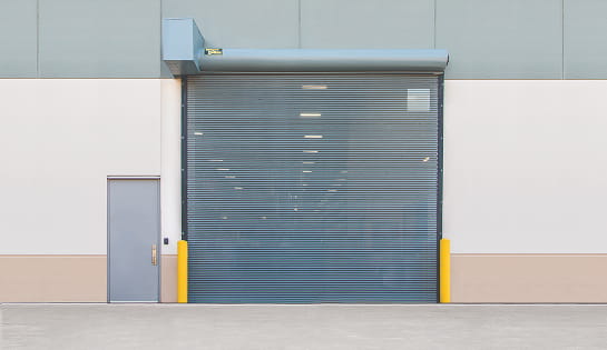 A vented rolling bug garage door preventing pests from coming in on the exterior of a warehouse facility.