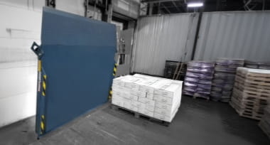 Blue dock leveler in a vertically stored position inside a warehouse loading bay