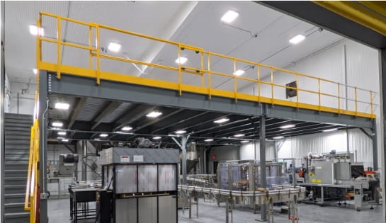 Gray industrial mezzanine installed above manufacturing machinery to maximize warehouse vertical space