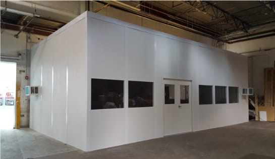 White modular office installed inside a warehouse near an open loading dock door