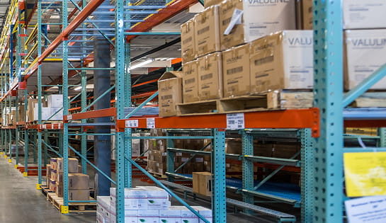 Warehouse storage aisle filled with boxes and cartons featuring horizontal rack labels for efficient inventory management
