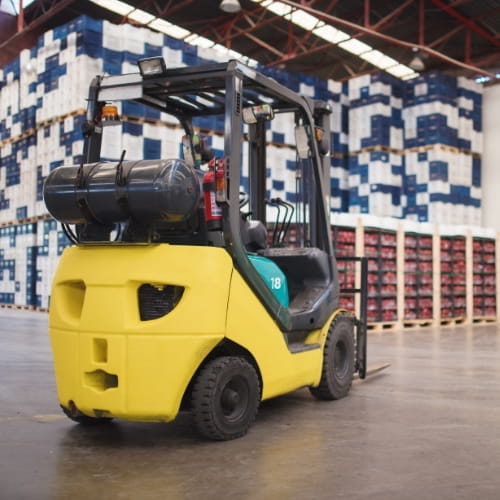 Yellow LP gas forklift parked in a warehouse aisle with storage racking behind it